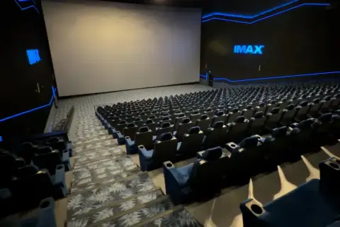 Pusta sala kinowa IMAX z ogromnym ekranem i rzędami niebieskich foteli. To właśnie co to znaczy IMAX w kinie – niesamowite wrażenia wizualne.