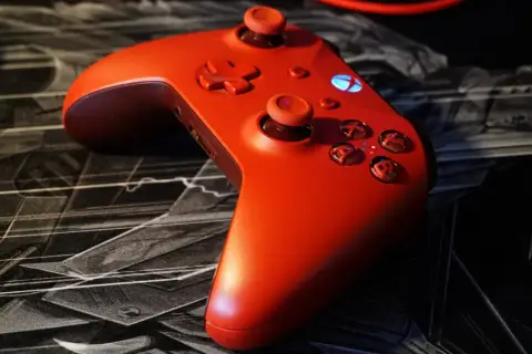 Czerwony kontroler Xbox na czarnej podkładce z motywem graficznym. Idealny do gry z nowym dlc.