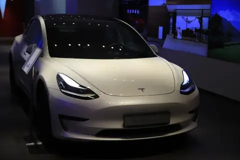 Biały samochód Tesla Model 3 z włączonymi światłami, prezentowany w salonie.