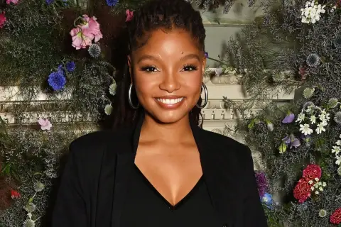 Halle Bailey ler mot kameran, omgiven av en blomsterinstallation.