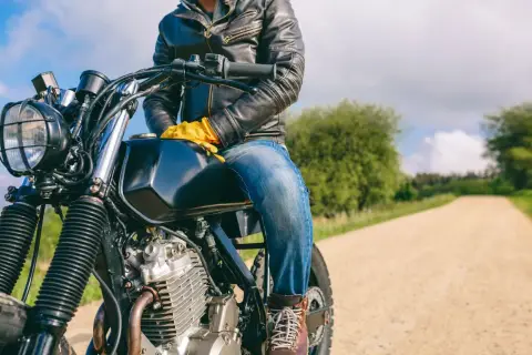 Motociclista con chaqueta de cuero y guantes amarillos, listo para la aventura. ¿Dyneema vs Kevlar? ¡La carretera espera!