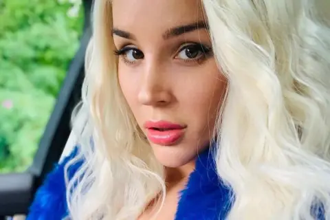 Blondynka w niebieskim futrze, zmysłowe spojrzenie. Ile lat ma sexmasterka? Trudno zgadnąć, wygląda młodo i pięknie.