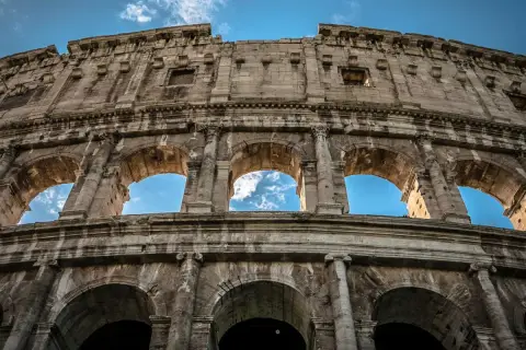 Il Colosseo visto dal basso, con il cielo azzurro e nuvole tra gli archi. Un'ottima meta per chi cerca come arrivare al Colosseo da Stazione Termini.