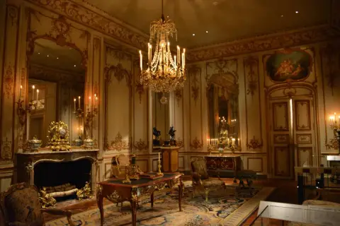 A lavish room with a crystal chandelier, ornate gold trim, and antique furniture embodies the royalcore aesthetic.