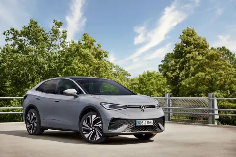 Szary VW ID.5 z czarnym dachem stoi na tle zielonych drzew i błękitnego nieba.