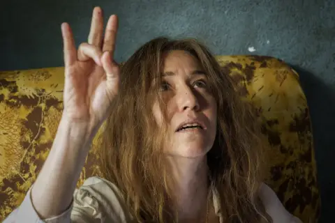 Irene Balmes, con el pelo revuelto, levanta la mano en un gesto místico.