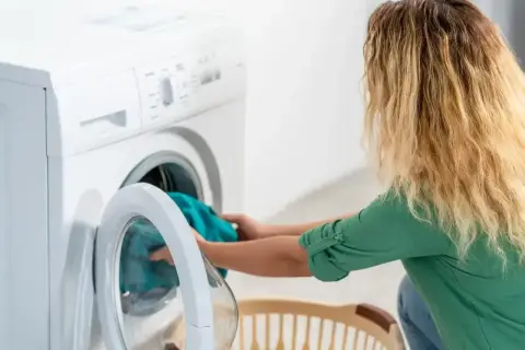 Kobieta wkłada pranie do pralki, która nie pobiera wody. Zmartwiona próbuje rozwiązać problem.
