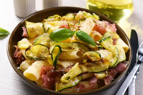 Makaron z cukinią i szynką parmeńską, ozdobiony bazylią. Idealne szybkie dania z cukinią na obiad.