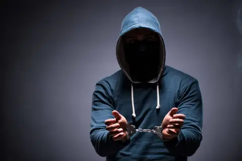Mężczyzna w kapturze i masce na twarzy, z rękami w kajdankach, symbolizujący zatarcie skazania i szansę na nowy początek.