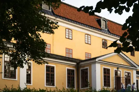Gula fasaden på Ulriksdals teater med tegeltak och mörkgröna trädgrenar som ramar in.