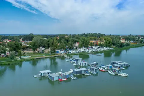 Nowoczesne houseboat'y unoszą się na spokojnej wodzie, obok kempingu z kamperami.