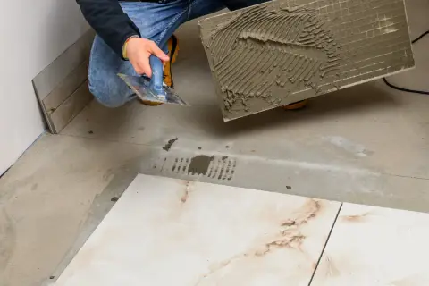 Układanie płytek 60x60 cennik. Majster z kielnią nakłada klej na płytkę, przygotowując ją do położenia na podłodze.