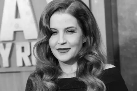 Lisa Marie Presley, w czerni, z falowanymi włosami i makijażem, na tle liter.