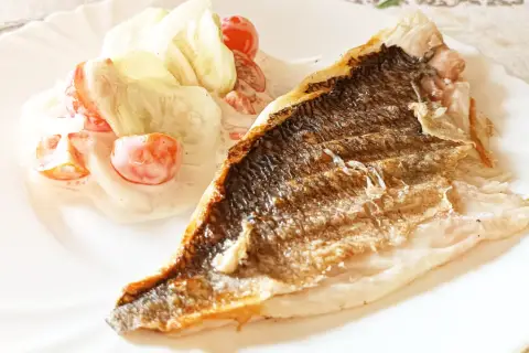 Dorada z grilla z chrupiącą skórką, podana z sałatką z pomidorków i ogórka w kremowym sosie.
