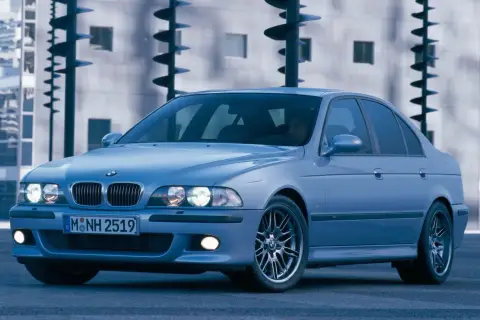 Błękitne e39 bmw z felgami M, zaparkowane przed nowoczesnym budynkiem.