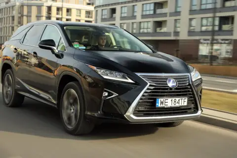 Czarny Lexus RX 450h jedzie ulicą w mieście, za nim widać nowoczesne budynki.