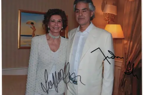 Sophia Loren and Andrea Bocelli pose for a photo, both with autographs on the image.