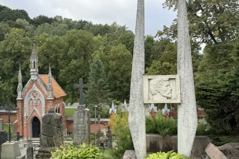 Kamienne obeliski i neogotycka kaplica na cmentarzu na Rossie. W tle zieleń drzew i pochmurne niebo.