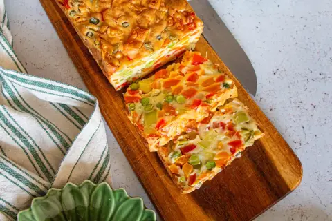 Tranches colorées d'une terrine de légumes savoureuse, garnie de poivrons, carottes et petits pois, prête à être dégustée.