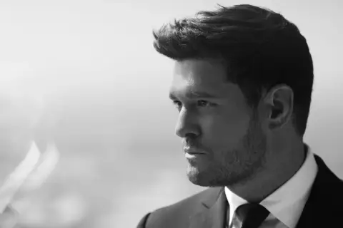 Michael Bublé w garniturze, zamyślony. Jego ponadczasowe michael bublé utwory brzmią jak jego spojrzenie.