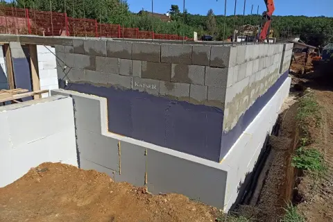 Izolacja fundamentów w starym domu w trakcie prac. Ściany z bloczków betonowych, styropian i hydroizolacja.