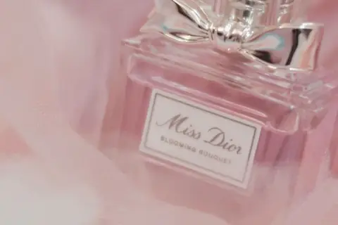 Frasco de perfume Miss Dior Blooming Bouquet, con un lazo plateado, sobre tela rosa suave. Un toque de elegancia para la madame de rosa.