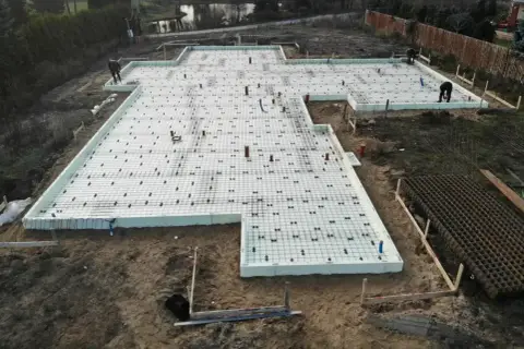 Budowa fundamentów z płyt izolacyjnych i zbrojenia. Szybki beton wkrótce zaleje tę konstrukcję, tworząc solidną podstawę.