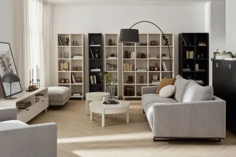 Nowoczesny living room z szarą sofą, regałami pełnymi książek i dekoracji, okrągłym stolikiem kawowym i lampą łukową.