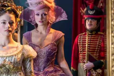 Trzy postacie z filmu "Dziadek do orzechów": dziewczynka w białej sukni, kobieta w fioletowej kreacji i żołnierz w czerwonym mundurze.