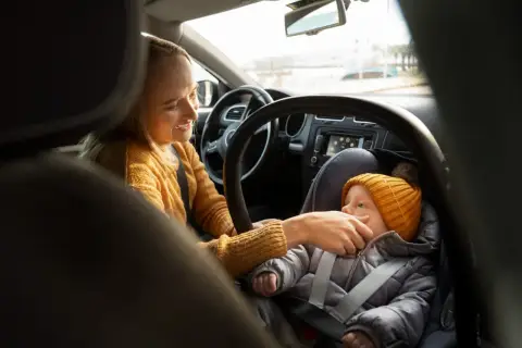 Uśmiechnięta mama przygotowuje dziecko do podróży. Podpowiadamy, jak ubrać dziecko do fotelika zimą, by było mu ciepło i bezpiecznie.