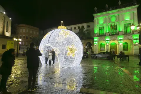 Una gran bola de luces ilumina la plaza en esta nit de cap d'any. Gente se hace fotos junto a la decoración.
