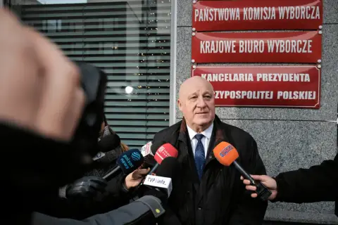 Mężczyzna przed Państwową Komisją Wyborczą, otoczony mikrofonami, mówi o prawdzie o finansowaniu kampanii PiS i decyzjach PKW o odebraniu dotacji.