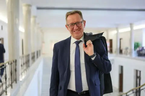 Uśmiechnięty mężczyzna w garniturze, który może być powiązany z pytaniem, dlaczego Robert Telus i Rafał Romanowski zostali zawieszeni w prawach członka.