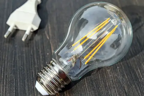 Żarówka LED i biała wtyczka na ciemnym drewnianym tle. Symbolizują potencjał, który czeka na aktywację, jak współczynnik jednoczesności w technologii.