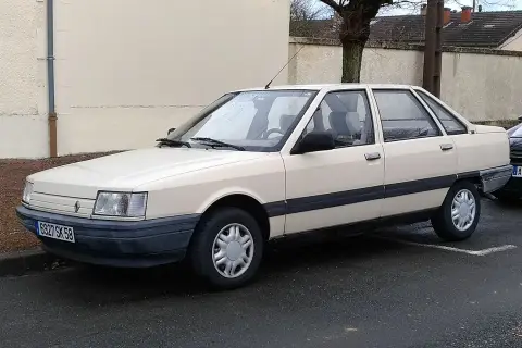 Jasny beżowy sedan Renault 21 z lat 80. stoi na mokrej drodze.