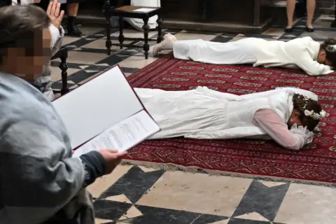 Dwie kobiety w białych sukniach leżą na dywanie w kościele. To uroczystość, podczas której zostają dziewicami konsekrowanymi.
