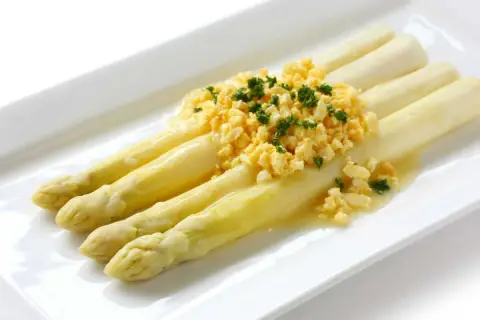 Asperges à la flamande : des asperges blanches tendres nappées d'une sauce savoureuse et garnies d'œufs brouillés et de persil frais.