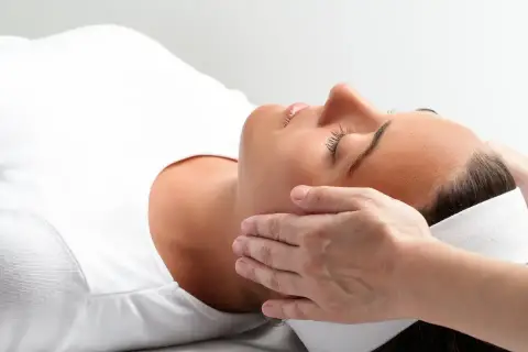 Kobieta w białej koszulce doświadcza relaksującego dotyku dłoni. To może być właśnie reiki co to za technika, która przynosi ukojenie.
