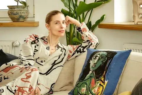 Katarzyna Zawadzka w domowym zaciszu, relaksująca się na kanapie obok poduszki z motywem Picassa. Jej życie prywatne pełne jest sztuki i spokoju.