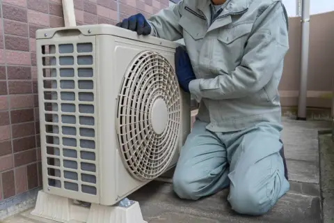 Pracownik w rękawiczkach sprawdza jednostkę zewnętrzną klimatyzacji. Wzór pozwolenia na montaż klimatyzacji w bloku jest kluczowy dla takich prac.