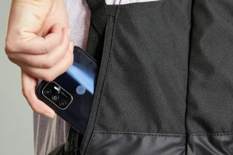 Dłoń wkłada telefon do bocznej kieszeni czarnego plecaka. Idealny, jaki plecak na rower, by mieć wszystko pod ręką.