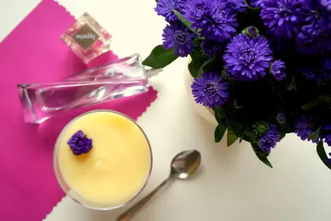 Perfumy "Hypnose" obok deseru i fioletowych kwiatów.
