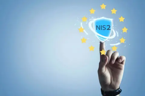 Palec wskazujący dotyka tarczy z napisem NIS2, otoczonej gwiazdkami Unii Europejskiej. Symbolizuje to bezpieczeństwo i zgodność z dyrektywą NIS2.