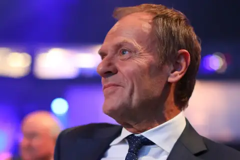Uśmiechnięty mężczyzna w garniturze, z lekko przerzedzonymi włosami. Czy Tusk jest rudy? Jego włosy mają odcień jasnego brązu.