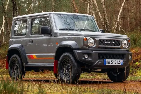 Szary Suzuki Jimny 2026 z kolorowymi pasami na boku, gotowy na terenową przygodę w lesie.
