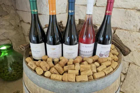 Pięć butelek wina, w tym różowe, na beczce pełnej korków. Idealne na tanie wino i wieczorne degustacje.