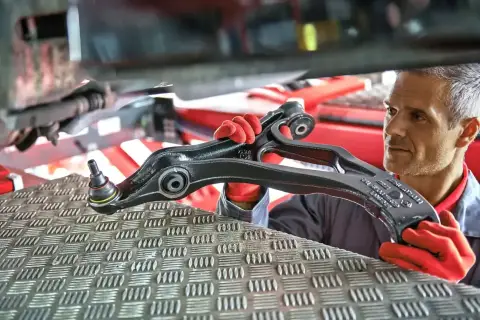 Mechanik w czerwonych rękawiczkach prezentuje element zawieszenia samochodu.