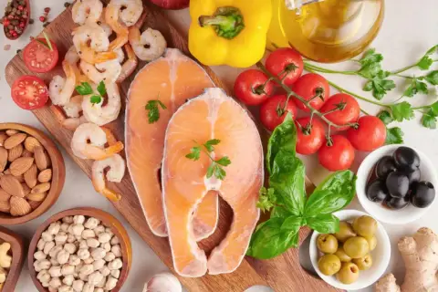 Salmón, camarones, almendras, garbanzos y aceitunas son algunos de los alimentos con yodo que se ven en la imagen, junto a tomates, pimientos y hierbas.