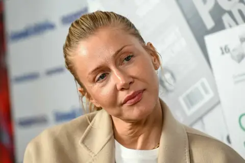 Katarzyna Warnke w beżowym płaszczu, z włosami upiętymi do tyłu. Aktorka znana z wielu polskich filmów.