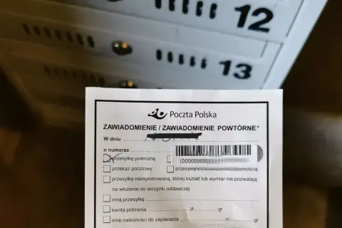 Zawiadomienie z Poczty Polskiej o przesyłce poleconej. W tle widoczne skrzynki pocztowe z numerami 12 i 13.
